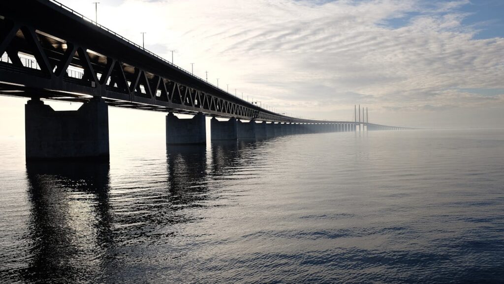 A stunning view of a large steel bridge reflecting on the tranquil water under a cloudy sky.